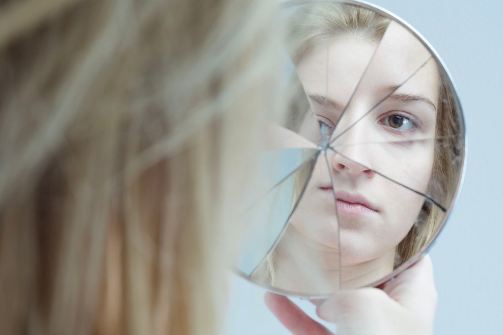 A woman looks at a broken mirror